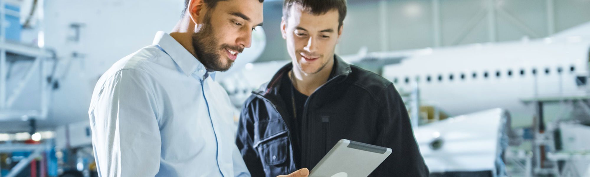 Aircraft Maintenance Worker and Engineer having Conversation. Holding Tablet.