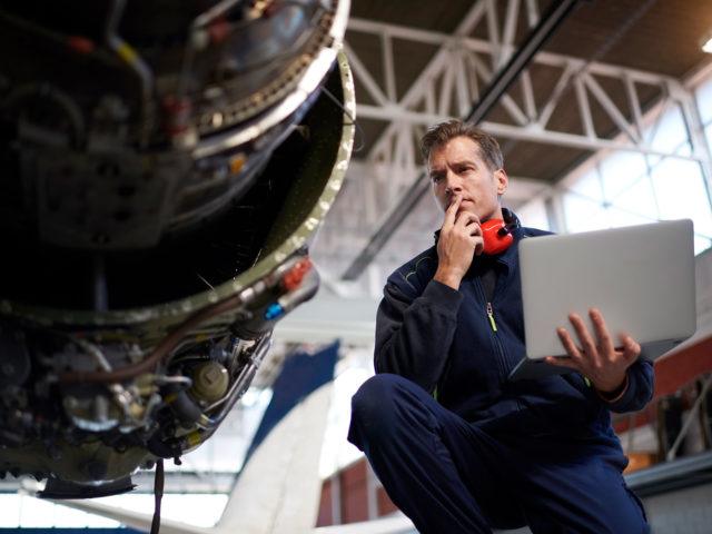 Aircraft engineer in the hangar holding laptop computer