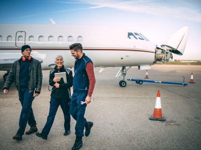 A team of aircraft engineers walking away from a small private jet with an opened nose cone parked on a taxiway