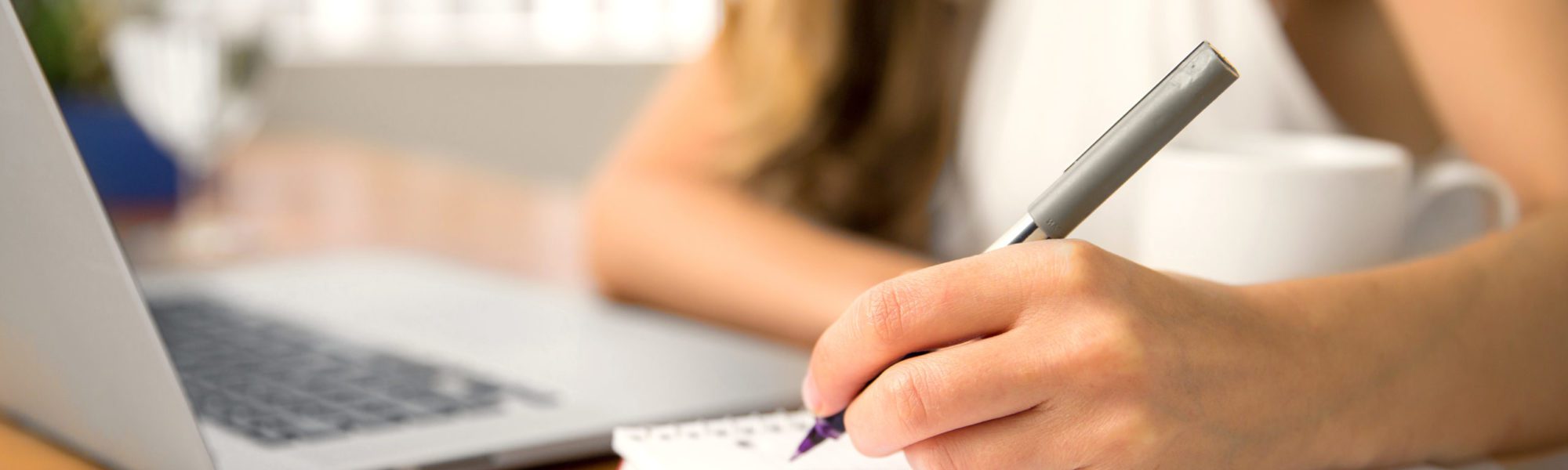 Hand pen coffee cup laptop table close up bokeh background taking notes Close-up of hand writing secretary executive business person personal assistant student